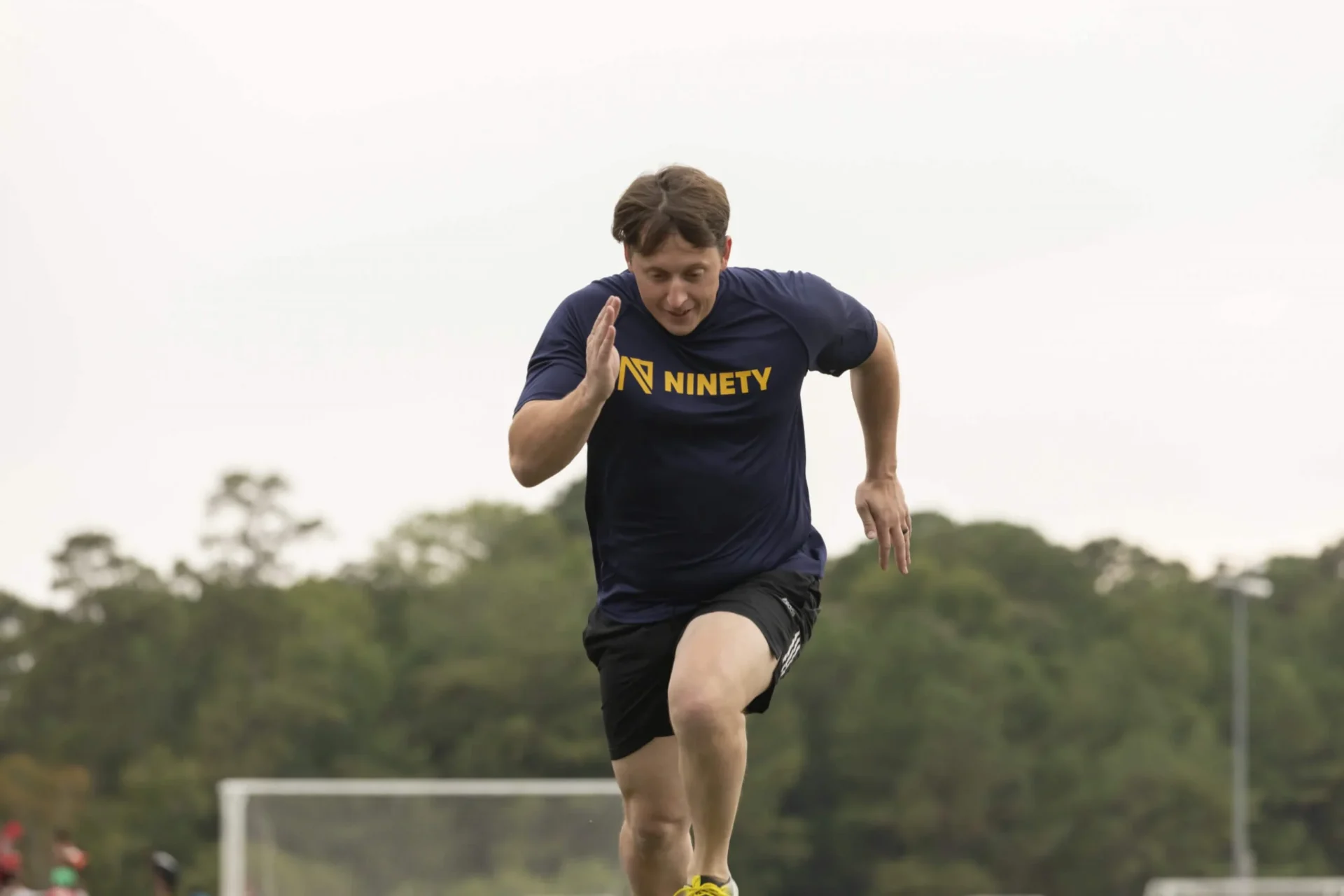 man in navy ninety shirt running on soccer field with trees in background