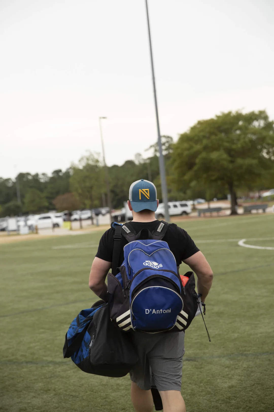 man with ninety cap soccer field rear view carrying lifestyle gear and adidas bag