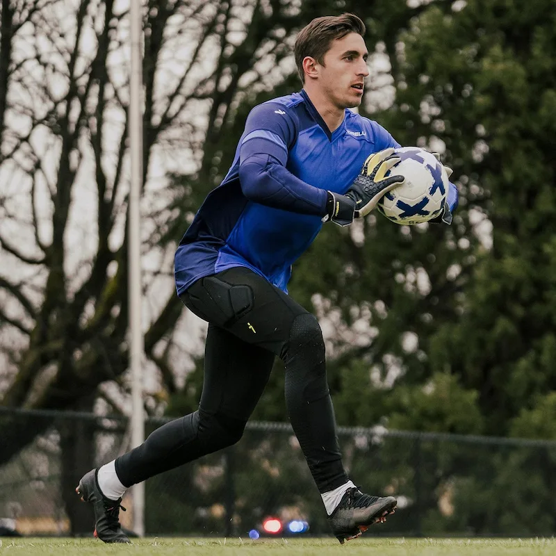 soccer goalkeeper in blue jersey catching a ball during practice